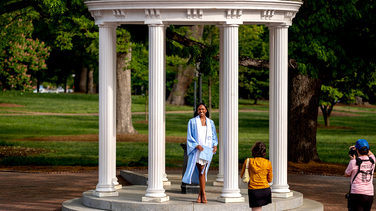 A person in graduate regalia poses for a photo at the Old Well.